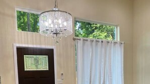 A living room with a dark door, a grey sofa with red cushions, a coffee table, and a chandelier. - Upscale Modern Private Cottage (Kirkland)
