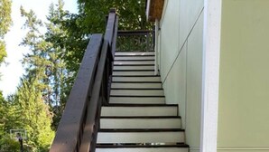 A staircase with wooden steps and a metal handrail, leading to a building with a light green exterior. - Upscale Modern Private Cottage (Kirkland)