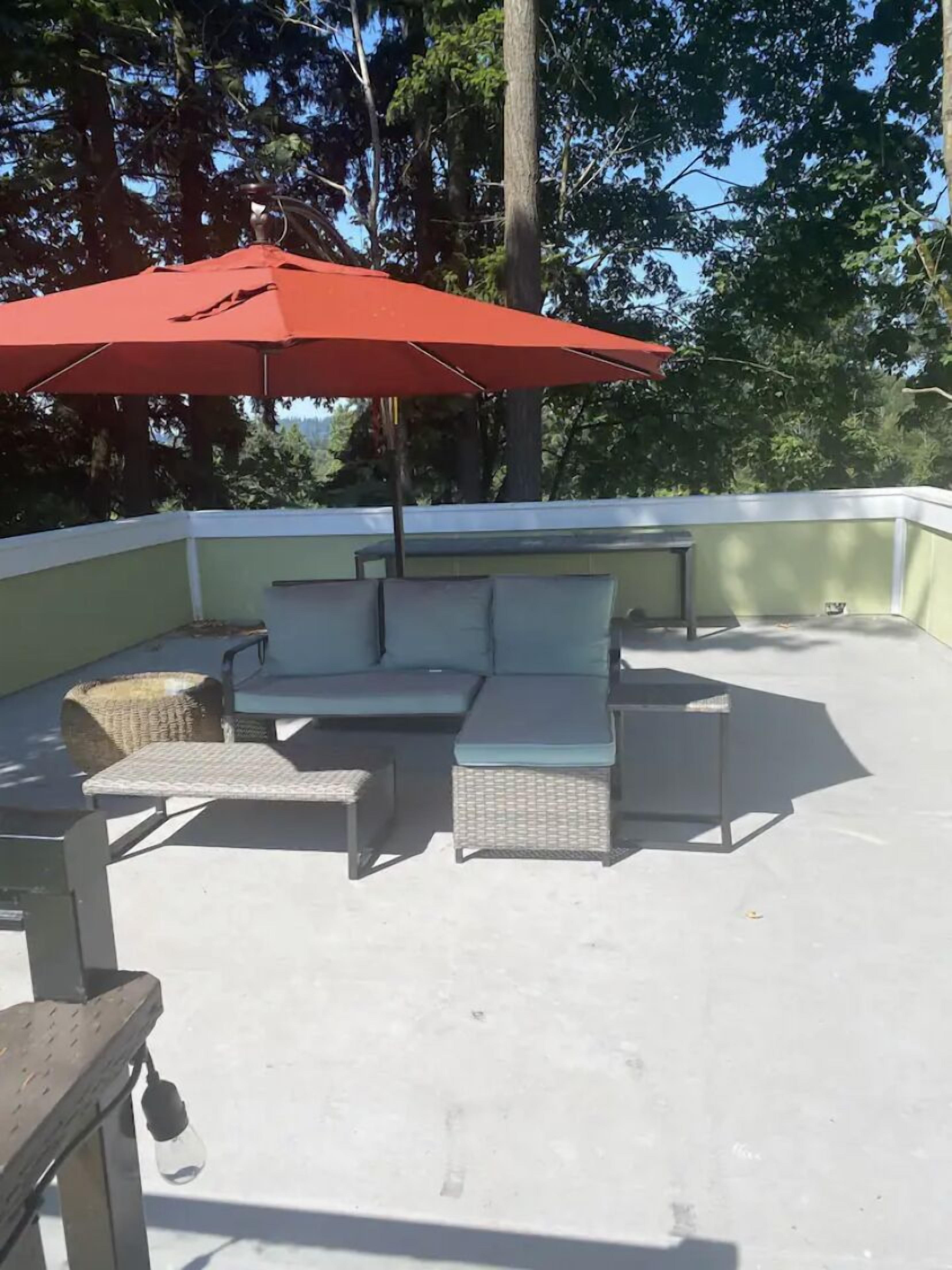 An outdoor patio with a red umbrella, a sectional sofa, and wicker chairs.
