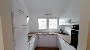 Une cuisine compacte avec des meubles blancs, un plan de travail en bois, un évier, une machine à café et un four.