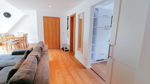 Un salon moderne avec un plancher en bois, un canapé marron, un coin repas avec des chaises et une table en bois, et une armoire blanche dont les portes sont ouvertes.