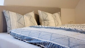Un lit bien fait, agrémenté d’oreillers à motifs et d’une couverture bleue et blanche.