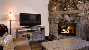 Una sala de estar acogedora con una chimenea de piedra, un televisor de pantalla plana sobre un soporte de madera y un sofá cómodo.