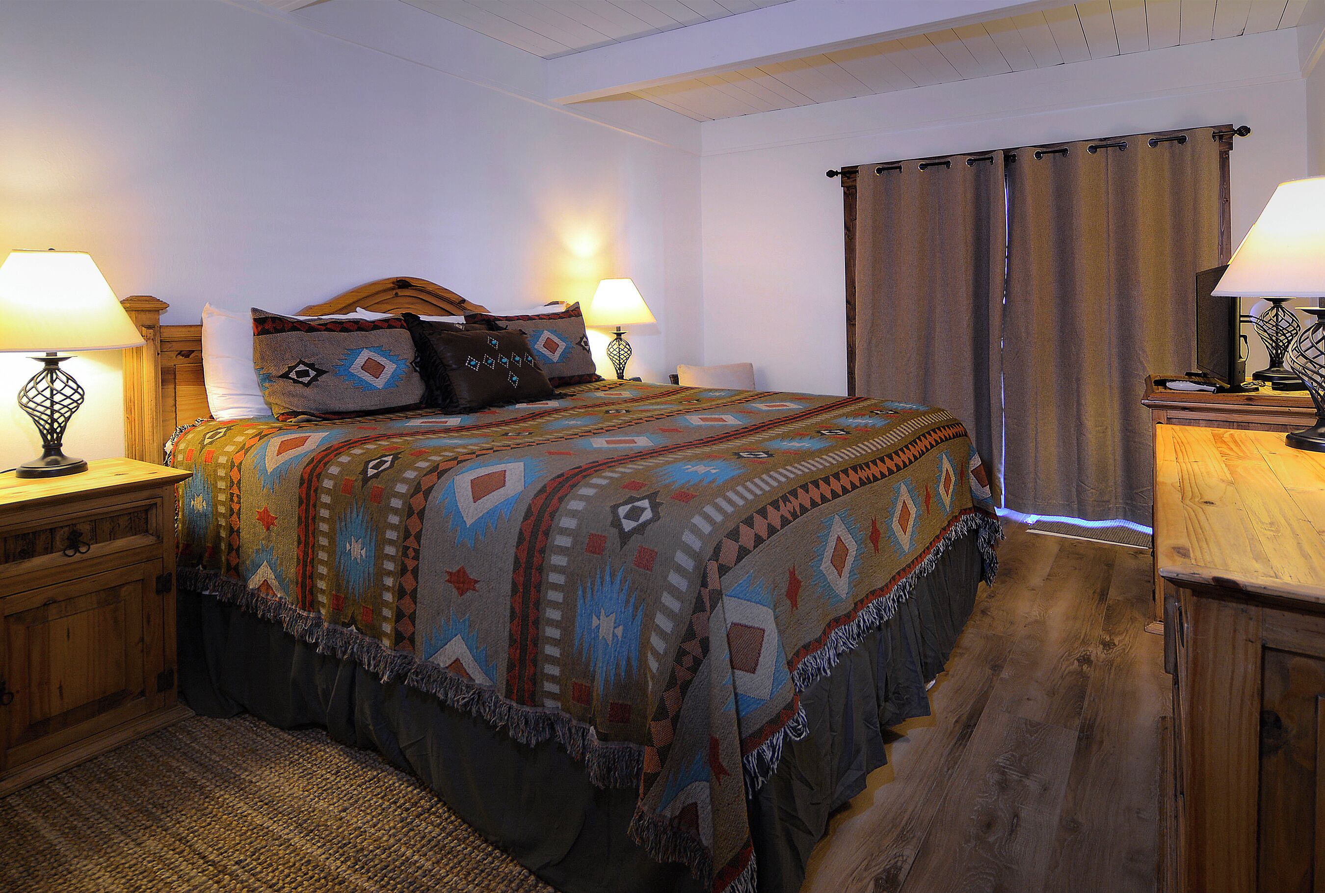 A neatly arranged bedroom with a large bed, two bedside tables with lamps, a wooden headboard, and a curtain on the window.