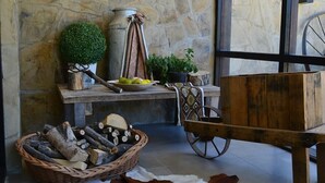 Un interior rústico con pared de piedra, chimenea, banco de madera, cesta de mimbre con leña y alfombra de cuero de vaca.