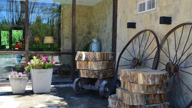 Un espacio al aire libre rústico con una estructura de rueda de madera, plantas en macetas y un muro de piedra.