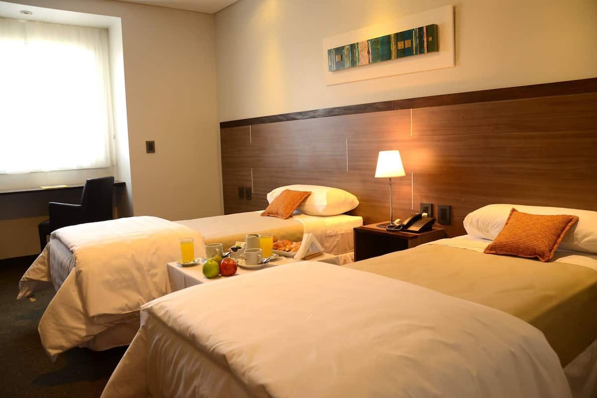 Ein Hotelzimmer mit zwei Betten, einem Nachttisch mit Lampe, einem Telefon und einem Frühstücksbrett mit Obst und Saft.