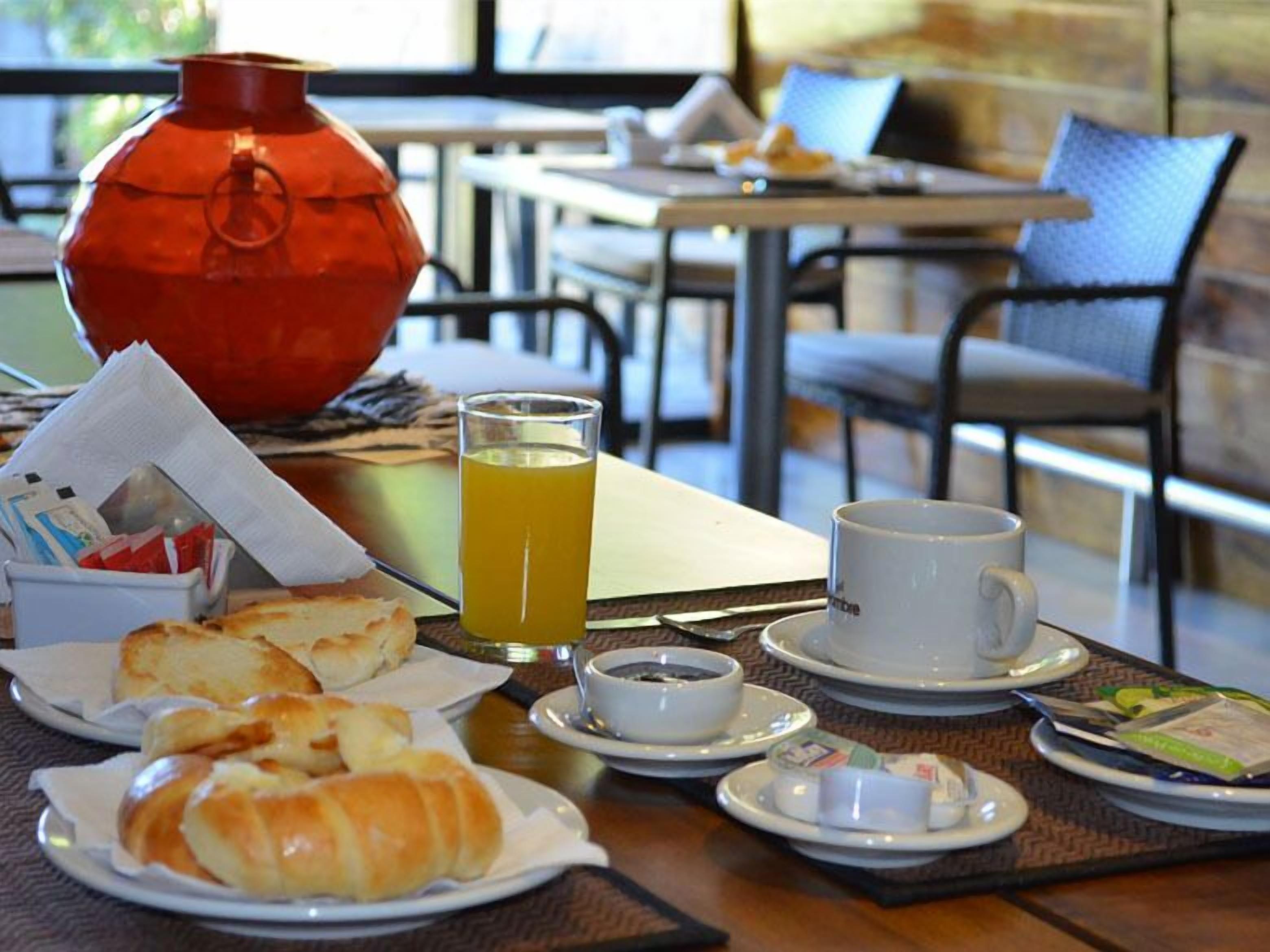 Une table mise pour le petit-déjeuner avec des croissants, un verre de jus d’orange, une tasse de café et un vase rouge.