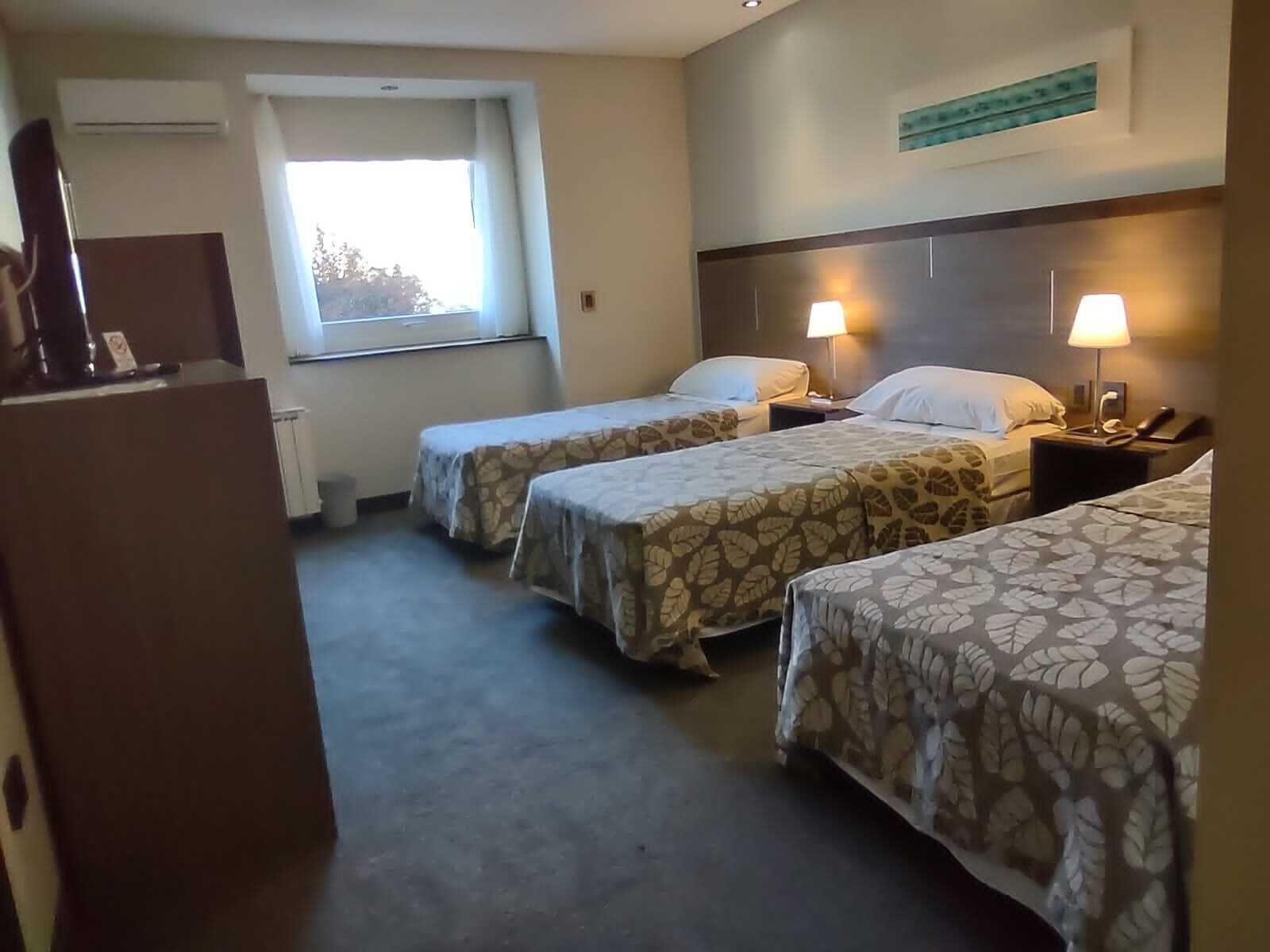 A hotel room with two single beds, a desk, a window, and a wall-mounted artwork.