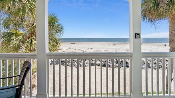 A beach view from a covered porch with a railing, palm trees, and a clear sky. - Oceanfront retreat, step onto the beach and a short distance to the Pier Village (Saint Simons Island)