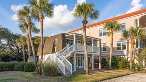 A two-story house with a porch, palm trees, and a sandy yard. - Oceanfront retreat, step onto the beach and a short distance to the Pier Village (Saint Simons Island)