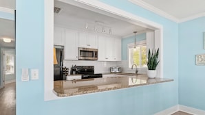 A modern kitchen with white cabinets, stainless steel appliances, and a granite countertop. - Oceanfront retreat, step onto the beach and a short distance to the Pier Village (Saint Simons Island)
