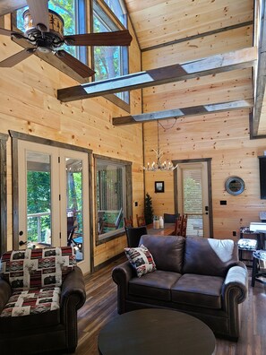Relax in this spacious room with a high ceiling, exposed beams, and a large window offering a view of the outdoors.