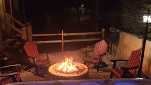 Een hottub met een vuurkorf in het midden, omringd door rode Adirondack stoelen.