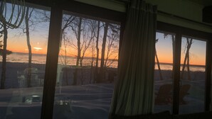 Een kamer met grote ramen met uitzicht op een besneeuwd landschap tijdens de zonsondergang.