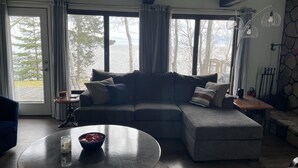 Een knusse woonkamer met een hoekbank, een ronde salontafel en uitzicht op een meer door grote ramen.