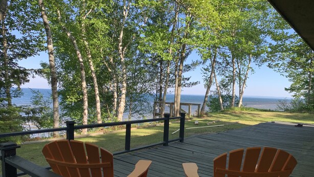 Een houten terras met twee Adirondack-stoelen en een kleine tafel, met uitzicht op een waterpartij en een bebost gebied.