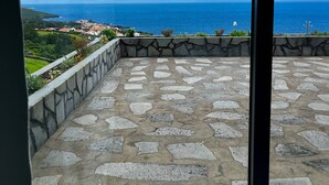 A balcony with a stone floor and a view of the ocean and distant landscape. - Casa  Rosa Chá  Pico (Açores - Ilha do Pico)
