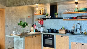 A modern kitchen with wooden beams, a built-in oven, and a polished concrete floor. - Casa  Rosa Chá  Pico (Açores - Ilha do Pico)