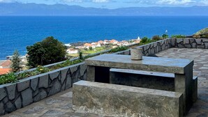 A patio with a stone wall and a bench overlooking a coastal view. - Casa  Rosa Chá  Pico (Açores - Ilha do Pico)