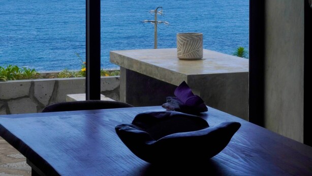 A room with a view of the ocean, a concrete bench, and a simple table with a bowl and a candle. - Casa  Rosa Chá  Pico (Açores - Ilha do Pico)
