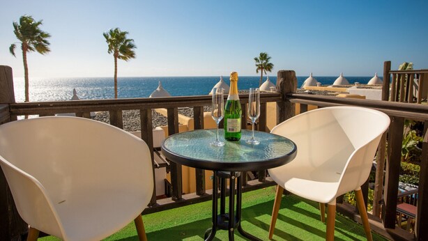A balcony with a table, two chairs, a bottle of champagne, and a view of the ocean. - Altamar 52 with balcony&pool By CanariasGetaway (San Bartolomé de Tirajana)