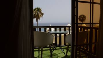 Un balcon avec une table et des chaises, donnant sur une plage et des palmiers.