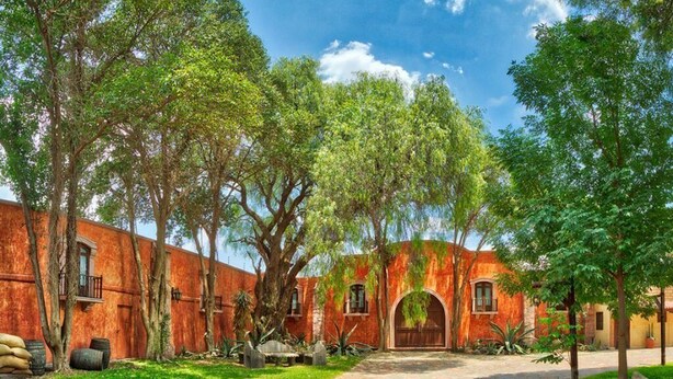 Un patio con un edificio de ladrillo rojo, un arco central y árboles circundantes.