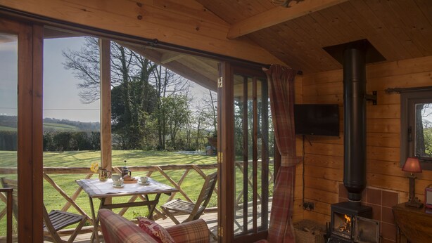 Uma cabana acolhedora com interior em madeira, um sofá, uma mesa com chaleira e uma lareira.