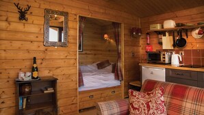 Interior acolhedor de uma cabana, com decoração em madeira, uma cama, uma kitchenette e uma área de jantar.