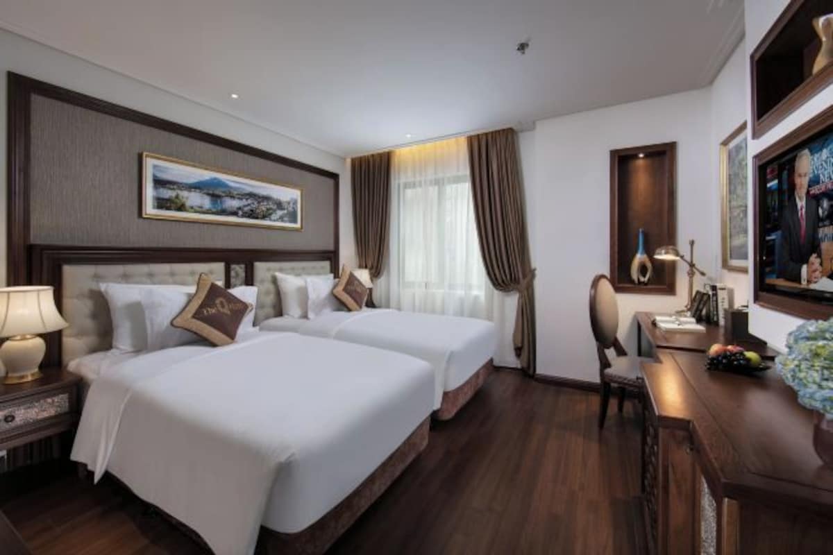 Habitación de hotel con dos camas, un escritorio, una silla, una lámpara y un cuadro en la pared.