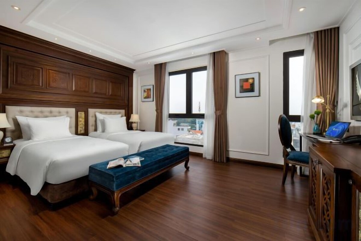 Een hotelkamer met twee bedden, een bureau, een stoel en een raam met gordijnen.