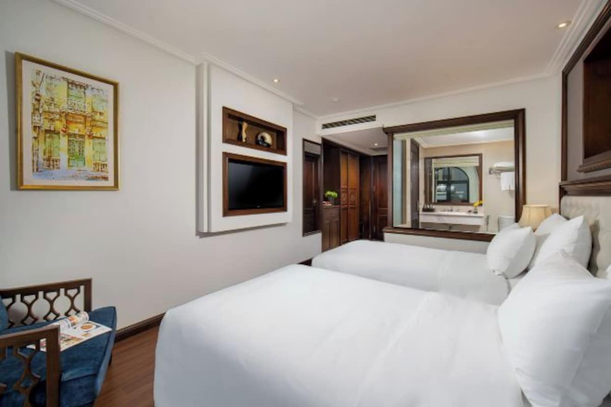 Una habitación de hotel con dos camas, un televisor, un cuadro y un espejo.