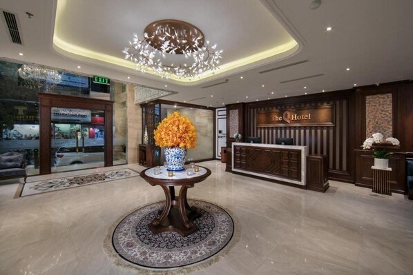 A hotel lobby with a reception desk, a large vase of flowers, and a chandelier. - The Q Hotel (Hanoi)