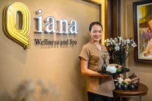A sign for 'Qiana Wellness and Spa' with a woman holding a tray of items. - The Q Hotel (Hanoi)