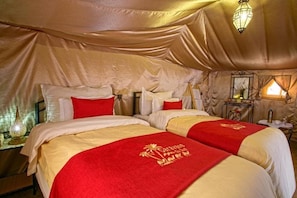A luxurious room with two beds, each with red and gold linens, and a large mirror on the wall.