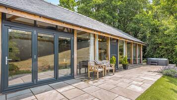 A modern house with large sliding glass doors, a patio with outdoor furniture, and a well-maintained garden.