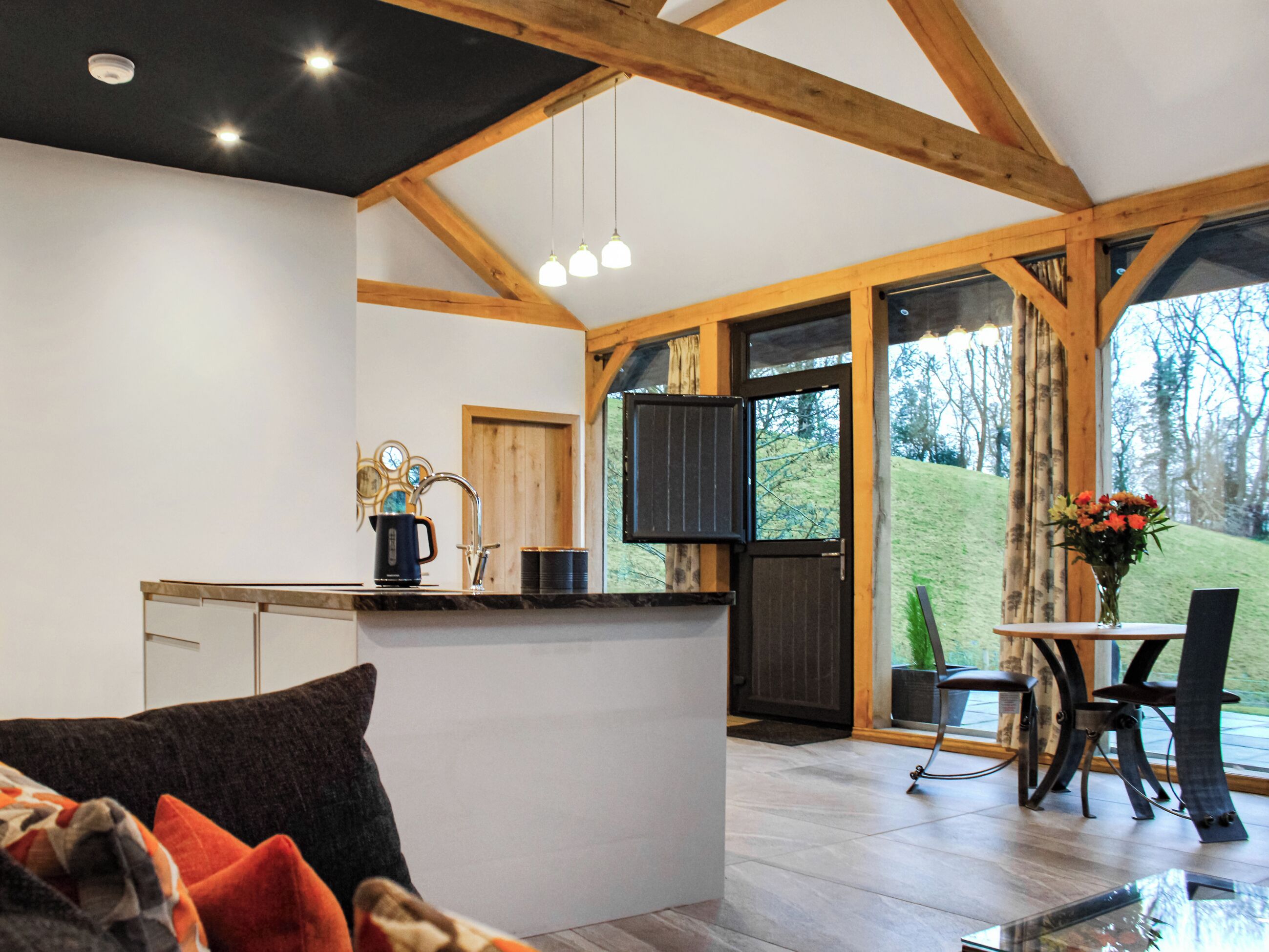 A modern kitchen with a central island, wooden beams, and large windows offering a view of the outdoors.