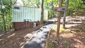 Una cabana amb la inscripció 'CABIN 3', un camí pavimentat que hi mena, i entorn arbres i una construcció de fusta.