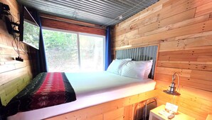 Habitació de fusta amb un llit, una tauleta de nit i una finestra.