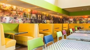 A brightly lit seating area with yellow and green upholstered chairs and tables, a wall adorned with various photographs, and a patterned floor. - Toy Story Hotel (Shanghai)