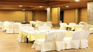 Une salle de banquet avec des tables rondes et des chaises blanches, chacune recouverte d’une nappe jaune.