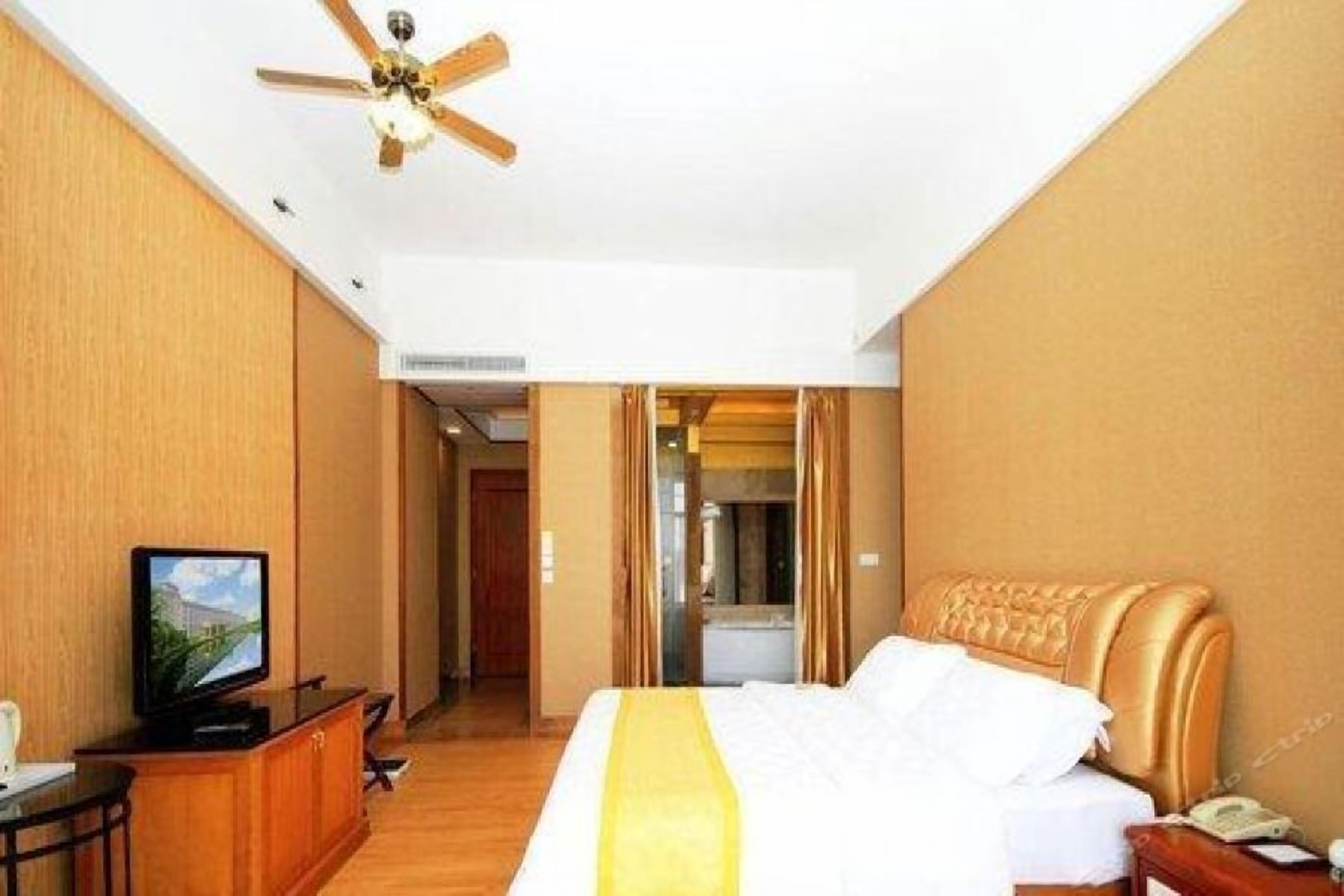 A hotel room with a bed, a television, a desk, and a ceiling fan.