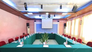 Une salle de conférence avec une longue table, des chaises rouges et un écran de projection.