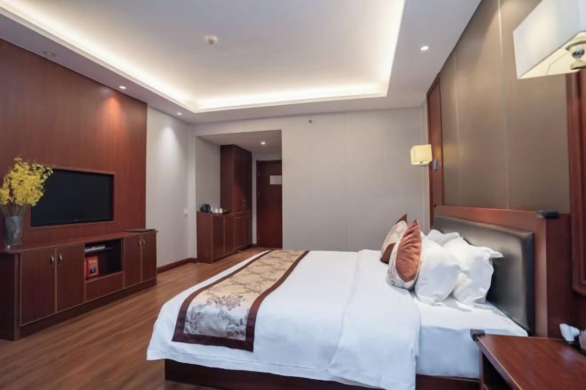 Una habitación de hotel con una cama grande, televisión, muebles de madera y una lámpara en el techo.