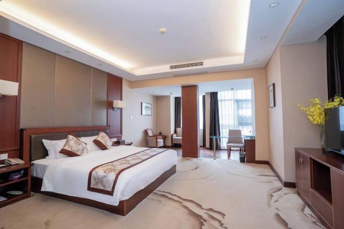 Una habitación de hotel con una cama grande, un escritorio, una silla y un televisor sobre un mueble.