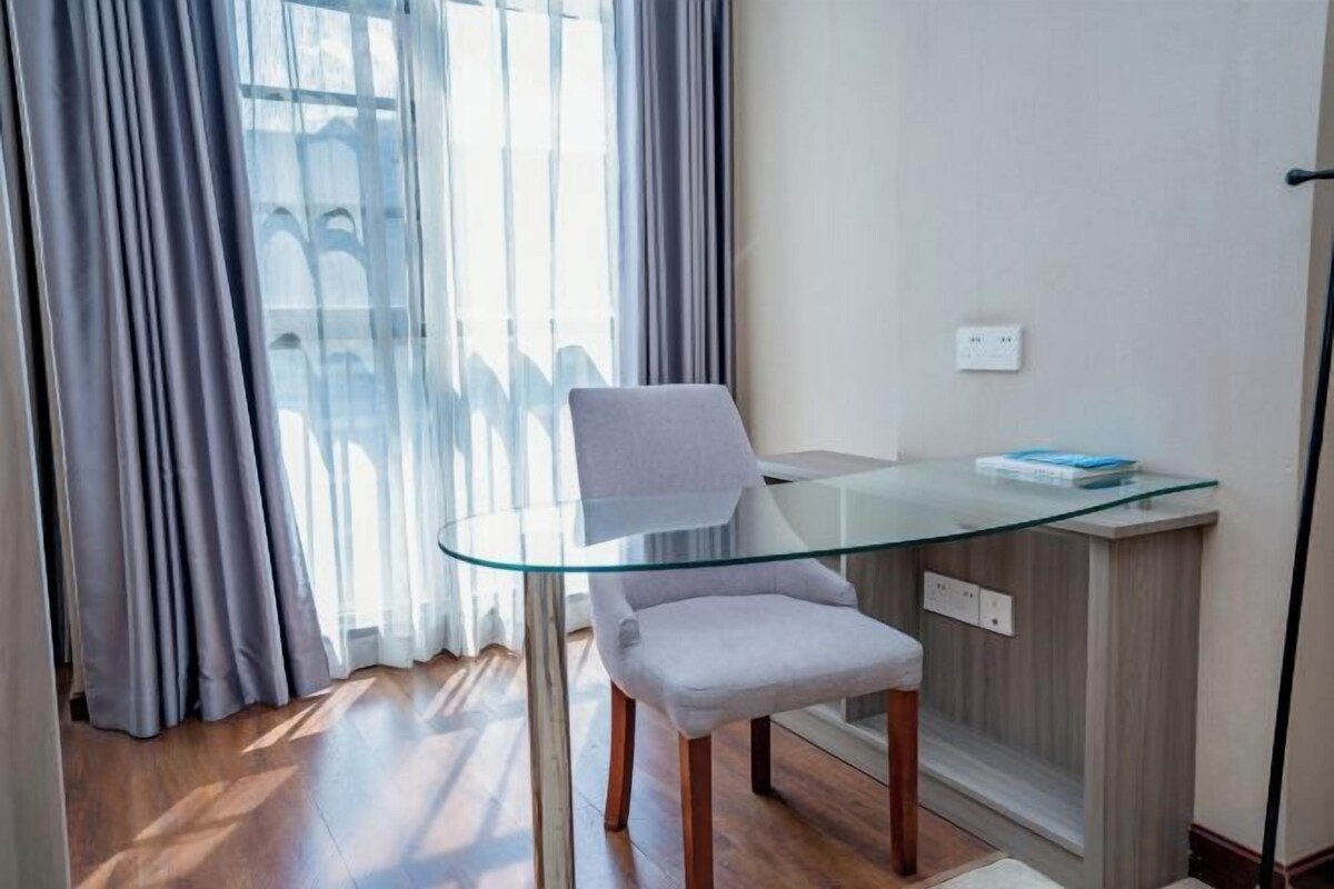 Una habitación moderna con una mesa de vidrio, una silla y vistas a través de una ventana con cortinas.