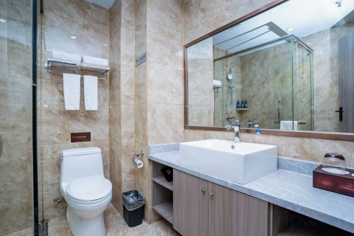 A modern bathroom with a marble wall, a large mirror, a white sink, and a toilet.