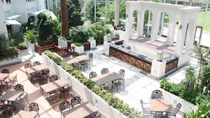 An indoor garden with tables and chairs, a central seating area, and a view of the surrounding greenery. - Grand Metropark Longxi Conference Center Beijing (Daxing)
