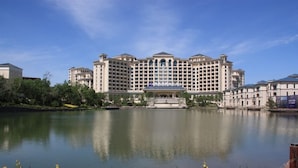 A large, multi-story hotel with a symmetrical facade, a central fountain, and a calm lake in the foreground. - Grand Metropark Longxi Conference Center Beijing (Daxing)